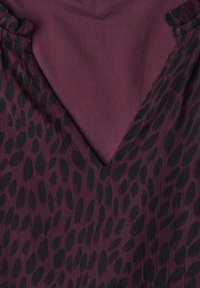 Gros plan d'un tissu bordeaux avec des taches noires irrégulières et un col en V.