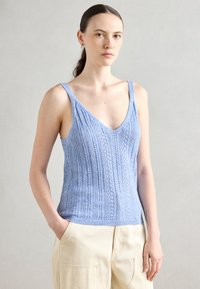 Lyseblå strikket tanktop med V-hals, med vertikal ribbestruktur og tynne stropper. Kombinert med beige høyhalsbukser.