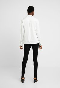 Vit långärmad skjorta med krage och bakfåll, i kombination med svarta strukturerade leggings och högklackade sandaler.