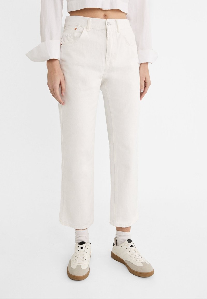 Bílé džíny s vysokým pasem a přímo střiženými nohavicemi, zapínané na knoflík, s pěti kapsami a jemnými švy. Kombinované s světle zbarvenými teniskami.