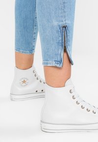 Lichtblauwe cropped jeans met een rits-uitsparing aan de zoom, gecombineerd met witte high-top sneakers met metalen oogjes en een logopatch.