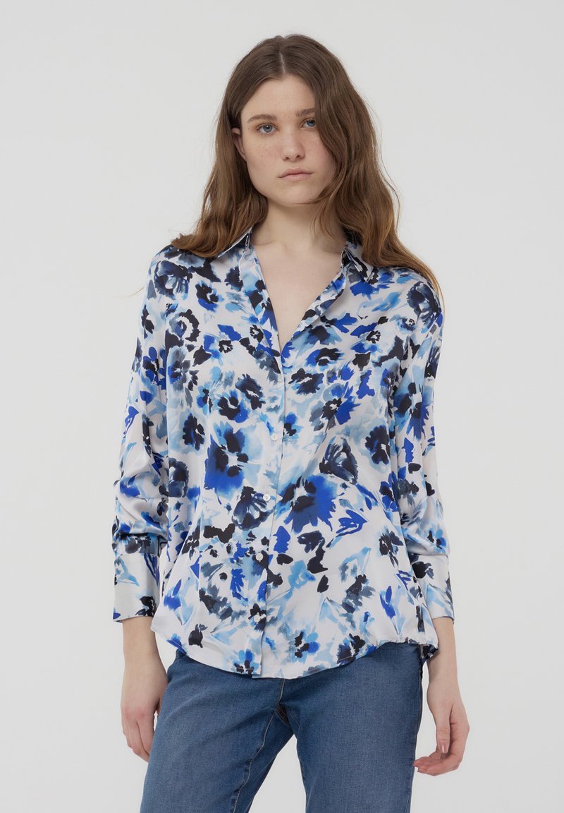 Camicia a fiori con bottoni in tonalità di blu e nero su uno sfondo chiaro; realizzata in un tessuto morbido e setoso, con maniche lunghe e colletto classico.
