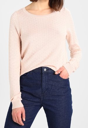 Light pink textured sweater with a round neckline and long sleeves, paired with dark blue high-waisted jeans featuring a button closure.