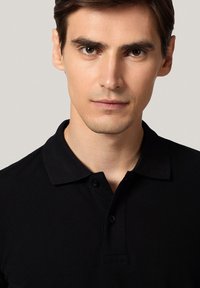 Czarna koszulka polo z kołnierzykiem, dwiema guzikami i teksturowanym materiałem. Zbliżenie na odzież, skupiające się na kształcie i detalach projektu.