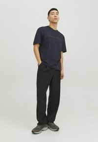 Marineblaues Baumwoll-T-Shirt mit kurzen Ärmeln und orangefarbenem Aufdruck, kombiniert mit schwarzen locker sitzenden Hosen und grauen Sportschuhen.