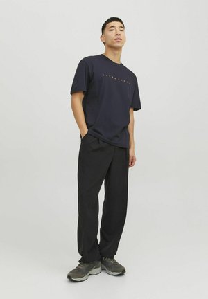 Navy cotton t-shirt with short sleeves and orange lettering, paired with black loose-fit trousers and gray athletic shoes.