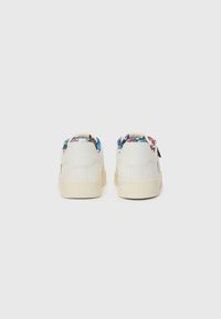 White sneakers with a textured surface, featuring a colorful patterned lining at the collar and thick cream-colored soles.