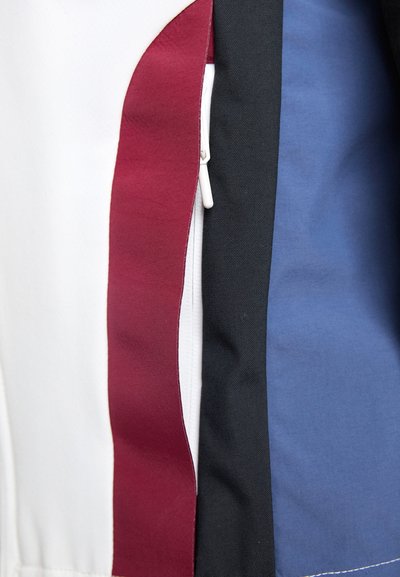 Îmbrăcăminte cu fermoar, prezentând secțiuni de țesături albe, burgundy, negre și albastre. Textură netedă cu culori contrastante și cusături îngrijite.