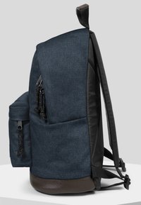Mochila de tejido azul oscuro con un acabado texturizado, que incluye un bolsillo lateral, correas ajustables y una base de cuero marrón.