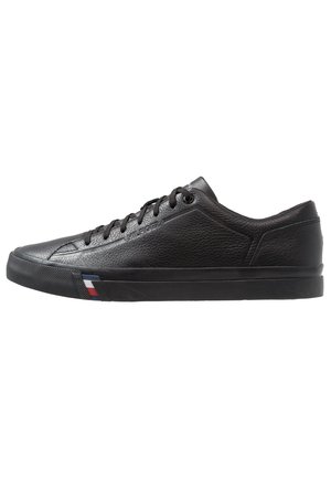 Baskets basses en cuir noir avec lacets noirs, panneau latéral texturé et détail rayé rouge, blanc, bleu sur la semelle près des orteils.