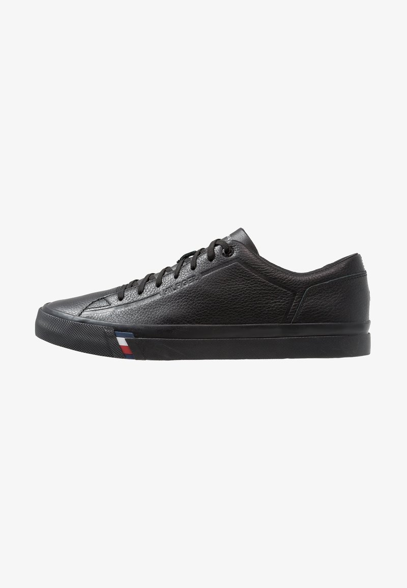 Baskets basses en cuir noir avec lacets noirs, panneau latéral texturé et détail rayé rouge, blanc, bleu sur la semelle près des orteils.
