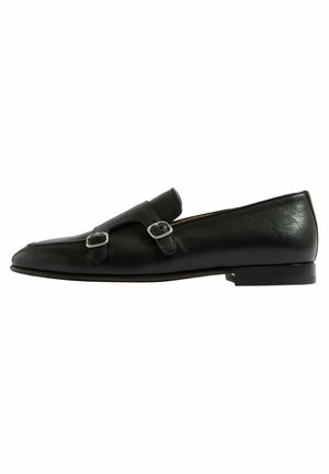 Mocasines de cuero negro con dos acentos de hebilla plateada, puntera afilada y tacón bajo. Textura lisa con detalles de costura mínimos.