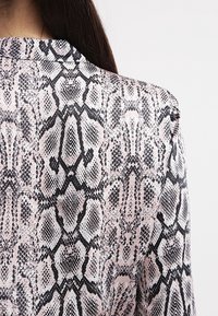Blusa stampata pitone con una texture liscia, caratterizzata da un motivo monocolore in nero e rosa in un design con colletto classico.