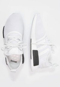 Vitaidsskor i vitt med meshövre, svarta detaljer på hälen, vita snören och tre vita ränder på sidan. "Boost"-logotyp synlig inuti.