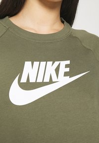 Grön sweatshirt med rund halsringning, med en stor vit "NIKE"-logga och en vit swoosh. Tyget verkar mjukt med en jämn textur.