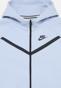 Φωτεινό μπλε φούτερ με φερμουάρ και μαύρο λογότυπο Nike, με σχεδιασμό σε σχήμα βέλους σε μαύρη λωρίδα και υφή υφάσματος με απαλή όψη.