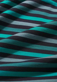 Artimųjų planas, kuris rodo minkštą audinį su horizontaliomis juostomis turkio, šviesiai mėlynos ir juodos spalvų. Matomos švelnios klostės ir tekstūros detalės.