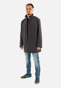Sort lang frakke med knapper, båret over en sort skjorte og lyseblå jeans. Skoene er mørkeblå med blå striber og en gummisål.