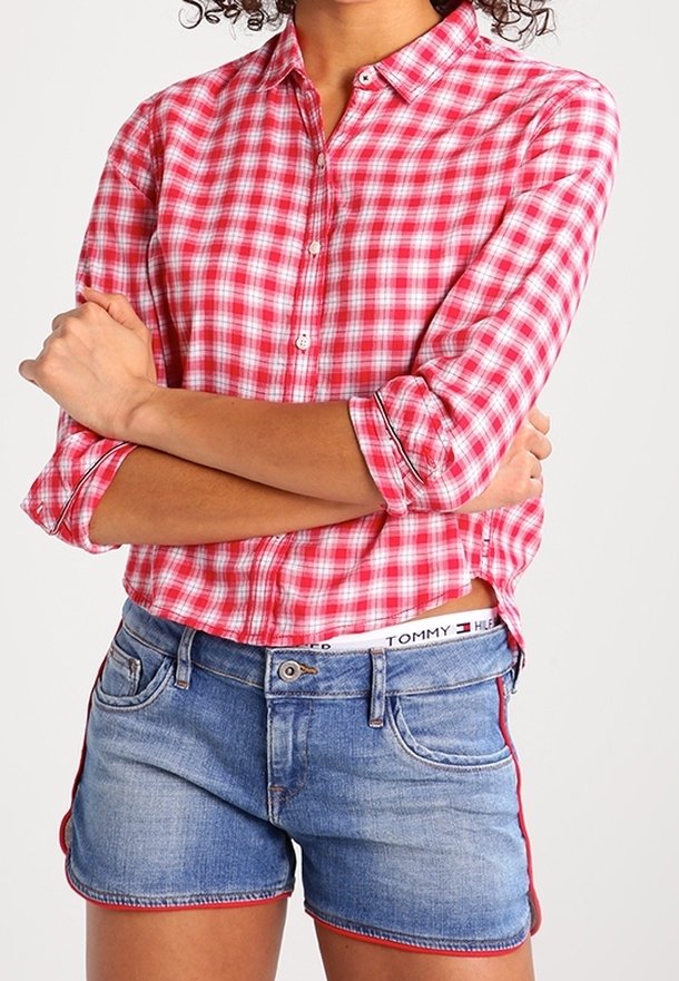 Rood en wit geruit overhemd met opgerolde mouwen, gecombineerd met blauwe denim korte broek met rode accenten aan de zijkanten.
