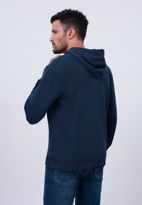 Plojna majica s kapuljačom u tamnoplavoj boji, izrađena od mekanog materijala, s dugim rukavima, kenguruba žepom i rebrastim manžetama.