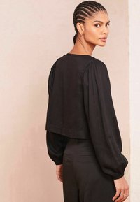 Sort cropped bluse med lange puffærmer, blødt stof og rund halsudskæring. Båret med skræddersyede sorte bukser.
