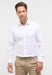 Witte overhemden gemaakt van gladde stof, met een puntige kraag, lange mouwen en een borstzak. Knopen in een bijpassende kleur.