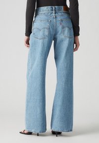 Ljust blå vida jeans i denim, med hög midja, två bakfickor och en brun läderlogga på midjebandet.