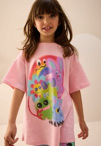 Rosa übergroßes T-Shirt mit bunten Cartoonfiguren und Designs, einschließlich einer Blume und einer lächelnden Katze. Weiches Baumwollmaterial.