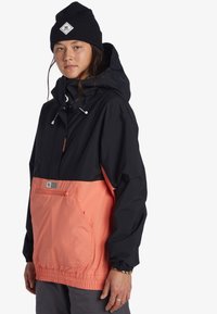 Čierna a koralová vodeodolná bunda s prednou kapsou, sťahovacou kapucňou a elastickými manžetami. Nosí sa s čiernym čiapkom.