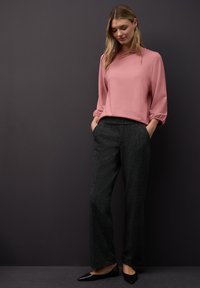 Różowa bluzka z długim rękawem ze ściągaczami, zestawiona z szerokimi spodniami o ciemnoszarym kolorze i teksturowanym wzorze oraz bocznymi kieszeniami. Całość uzupełniają czarne baleriny.