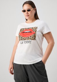 T-shirt en coton blanc avec un graphique de lèvres rouges sur un fond de motif léopard, accompagné du texte "LA FEMME" en noir. Manches courtes, coupe décontractée.