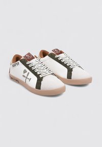 Zapatillas blancas con detalles en verde oliva, detalles en cuero marrón y cordones con estampado. Material texturizado con diseño bajo, suela plana beige.