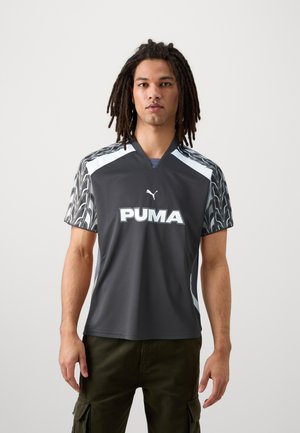 Maillot de sport gris avec un col en V, présentant des manches à motifs noir et bleu. Grand logo "PUMA" blanc sur le devant. Fabriqué en tissu léger.