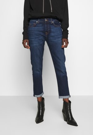 Dark blue rolled-up cuff jeans worn with black pointed-toe heeled ankle boots and a black long-sleeve top.
