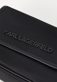 Clutch preto em nylon com um acabamento texturizado, apresentando um proeminente logótipo em relevo "KARL LAGERFELD" na parte da frente e elegantes detalhes de costura.