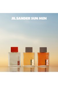 Three glass perfume bottles in varying shades: clear, yellow, and amber, each with square tops and bold "JIL SANDER SUN MEN" labels.