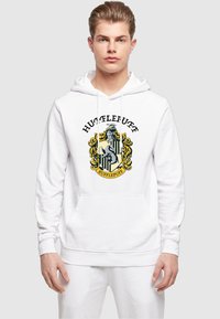 Fehér kapucnis pulóver zsinórokkal, középen egy színes Hufflepuff címerrel. Puha, textúrált anyagból készült. Elülső zsebbel.