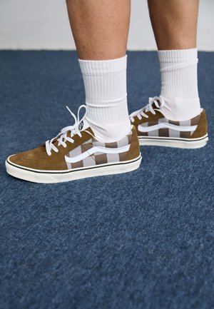 Sneaker in suede marrone con pannelli bianchi a scacchi, lacci bianchi e suole in gomma, abbinate a calzini bianchi a coste.