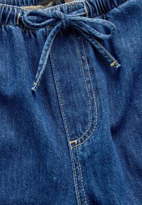 Zilā denim bikses ar aukliņu viduklī, ar kontrastējošu beigu šuvumu un mazu priekšējo kabatu. Mīksta tekstūra ar mērenu stiepšanos.