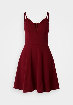 Burgundy A-line dress with thin adjustable straps, plunging V-neck, fitted bodice, and flared skirt, made from a smooth fabric.