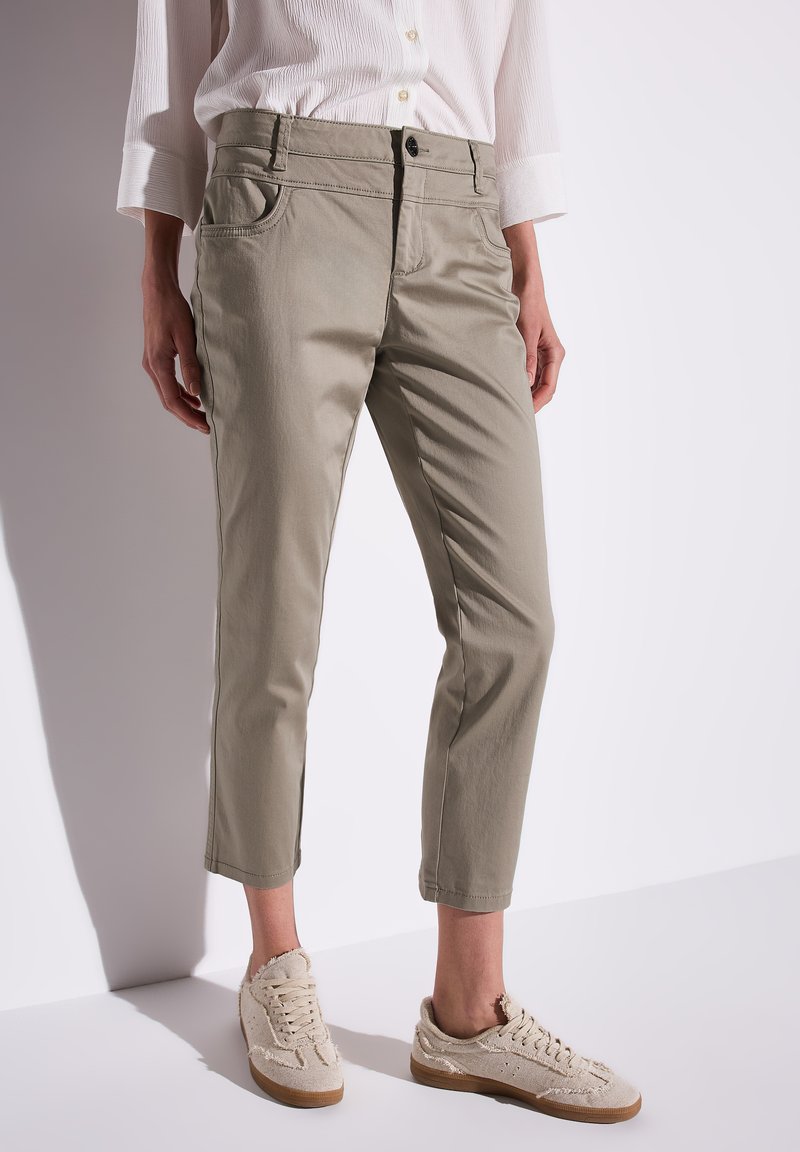 Ljusbeige chinos med smal passform, uppvikta anklar och framfickor. Bärs tillsammans med off-white strukturerade sneakers.