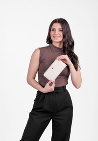 Světle růžová kožená peněženka se zlatými doplňky, obdélníkového tvaru, s logem na přední straně, kterou drží osoba v hnědém topu.