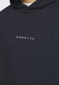 Tmavě modrá mikina s kapucí vyrobená z měkkého materiálu, s vysoce kvalitním texturovaným vyšívaným logem "MENNACE" v kontrastní bílé barvě. Jednoduchý design, bez dalších vzorů.