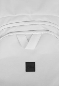 Zaino bianco realizzato in tessuto testurizzato, dotato di un'etichetta nera a contrasto con la scritta "URBAN CLASSICS" e due tasche orizzontali con zip.