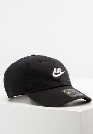 Czarna czapka bejsbolowa Nike z białym haftowanym logo i regulowanym paskiem, leżąca na białej powierzchni na jednolitym tle.
