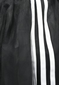 Čierna tylová látka s vertikálnymi bielymi pruhmi. Ľahká, polopriehľadná textúra. Pruhy sa na odeve menia na šírku.