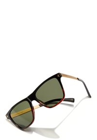Square-shaped sunglasses with black and tortoiseshell frames and green lenses, featuring gold temples and "Designed in Spain" text.