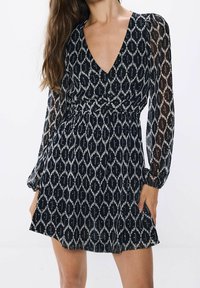 Robe à motifs noir et blanc avec manches longues en voile, un décolleté en V et une taille ajustée, dotée d'une jupe ludique et d'une texture subtile.