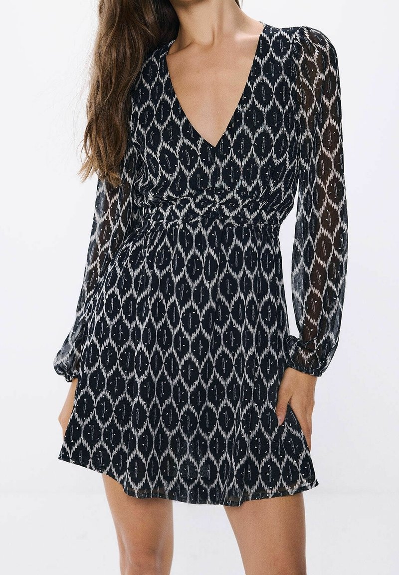 Robe à motifs noir et blanc avec manches longues en voile, un décolleté en V et une taille ajustée, dotée d'une jupe ludique et d'une texture subtile.