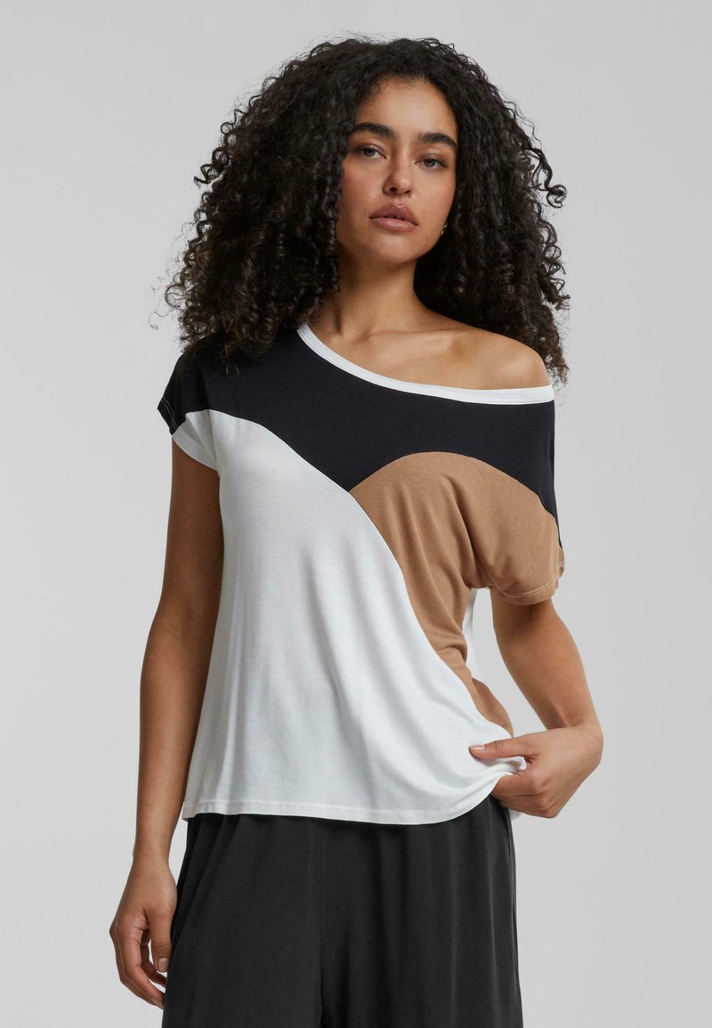 T-shirt asymétrique avec des blocs de couleur noirs, blancs et beiges ; tissu doux ; encolure large ; manches courtes ; coupe décontractée.